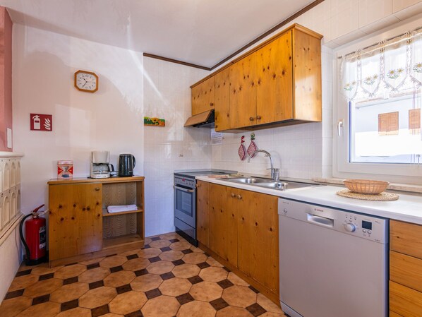 A compact kitchen with wooden cabinets, a built-in oven, a dishwasher, and a window with curtains. - Cesa Micheluzzi (CZI712) by Interhome (Canazei)