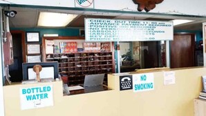 A store interior with a sign indicating check-out time, advance payment, and no personal checks. - Robinhood Motel Anaheim West (Anaheim)