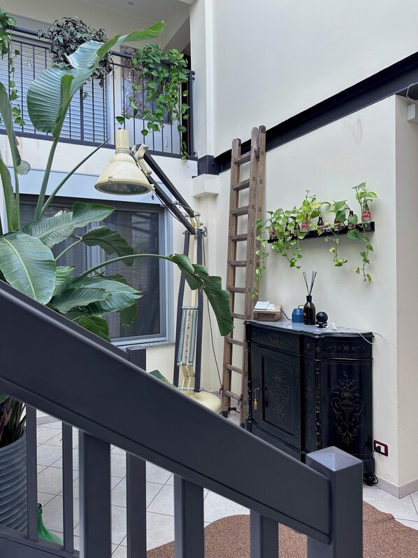 A multi-level balcony with potted plants, a ladder, and a hanging light fixture. - OMA Residence (Pavia)