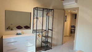 A modern bedroom with a wooden ceiling, a large mirror, a white bed with towels, a wardrobe, and a bathroom with a shower. - OMA Residence (Pavia)