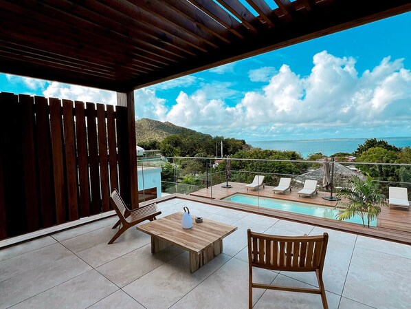 A modern outdoor pool area with a wooden deck, lounge chairs, and a table.