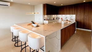 Una cocina moderna con una isla de mármol, taburetes de bar, armarios de madera e iluminación empotrada.