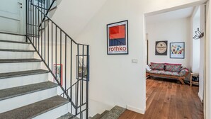 Eine Treppe mit schwarzen Geländern führt zu einem Wohnbereich mit einer Couch und Holzboden.