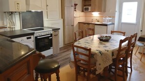 Una cucina compatta con piano cottura, forno, microonde e lavello. C'è un tavolo da pranzo con sedie e una ciotola sopra.