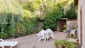 Un'area patio con tavolo e sedie, circondata dal verde e da un vialetto ghiaioso.