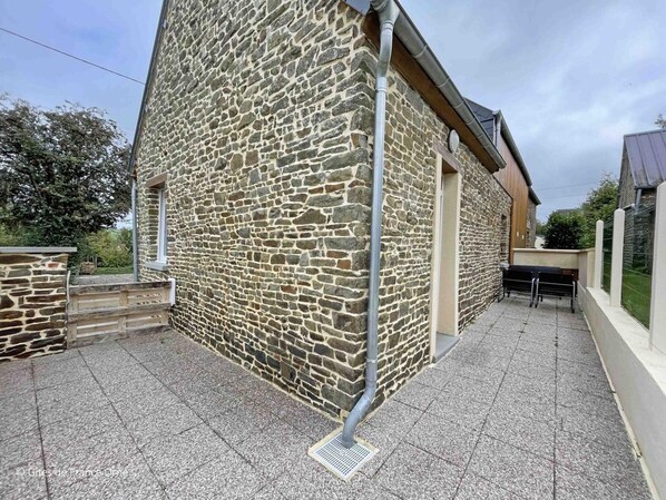 A stone building with a tiled patio, a bench, and a metal gutter.