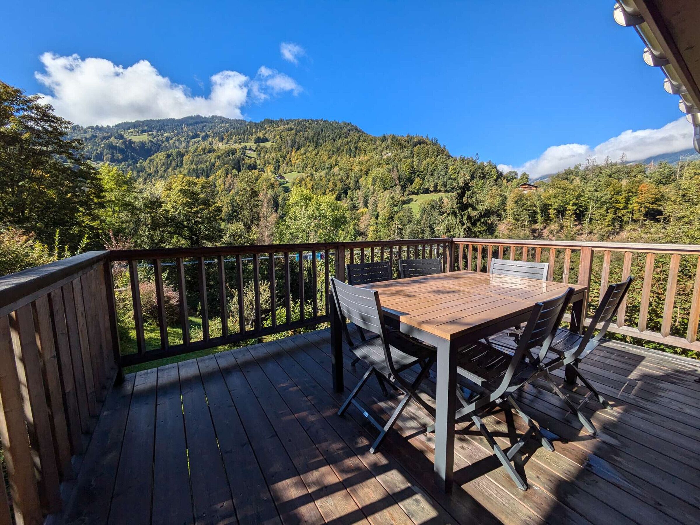 Una terraza de madera con una mesa y sillas, con vista a un paisaje montañoso.