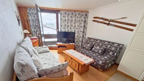 En stue med en sofa, et træbord, et fjernsyn og et ski stativ på væggen.