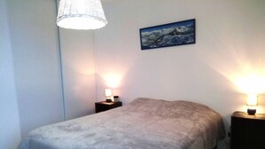 Un dormitorio con una cama, dos mesitas de noche con lámparas, un cuadro colgado en la pared y una lámpara colgante.