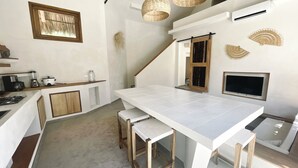 Une cuisine moderne avec des meubles blancs, un grand îlot central doté de tabourets, une cuisinière encastrée et un luminaire suspendu.