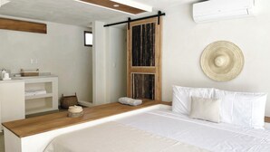 Une chambre moderne avec une tête de lit en bois, un grand lit recouvert de draps blancs, une petite table de chevet avec un panier, et un climatiseur fixé au mur.