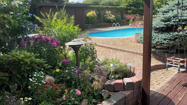 Ein Garten mit Schwimmbecken, umgeben von verschiedenen Pflanzen und Blumen.