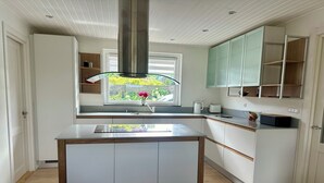 Eine moderne Küche mit Kochinsel, weißen Schränken und einem Fenster mit Blick auf Grünflächen.