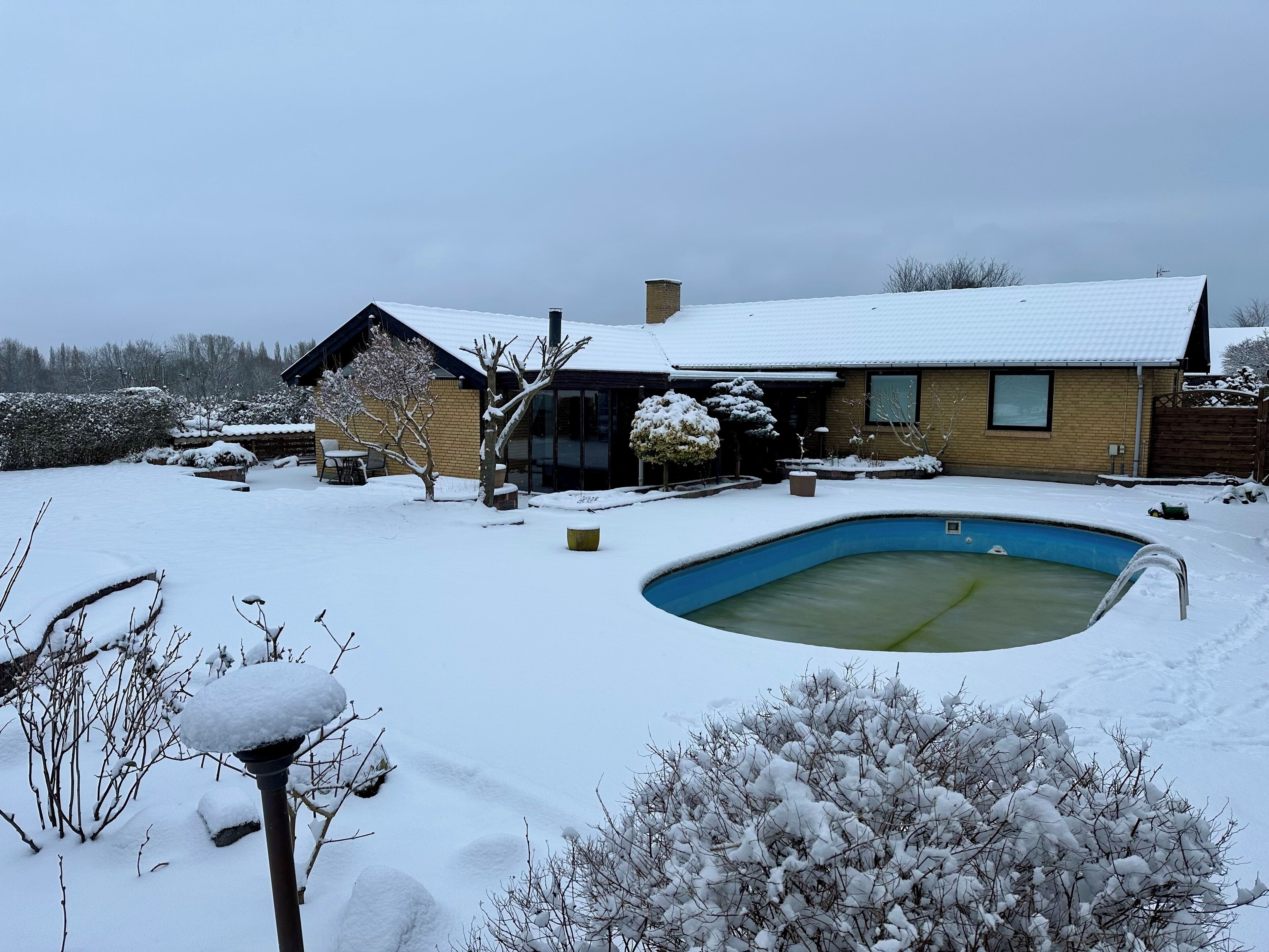 Une maison avec une cour enneigée, une piscine et une terrasse en bois.