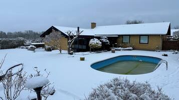 Une maison avec une cour enneigée, une piscine et une terrasse en bois.