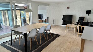 Ein modernes Wohnzimmer mit einem Holzesstisch, weißen Stühlen, einem schwarzen Sofa, einem Kamin und einem Fernseher.