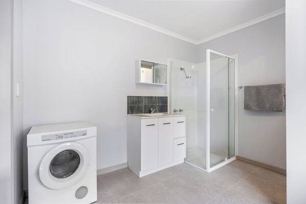 Un baño moderno con lavadora, cabina de ducha de vidrio y suelo de baldosas.