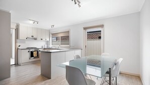 A modern kitchen with white cabinetry, a central island, and a glass dining table with chairs.