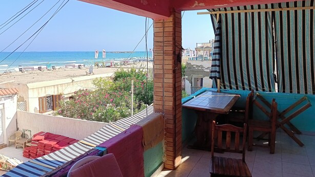 Un balcón con vista a la playa, una mesa con sillas y cojines de colores.