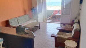 Habitación con sofá, una mesita, ventilador y vista a la playa a través de una puerta abierta.