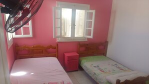 Un dormitorio con dos camas de madera, una pared rosa y una ventana con contraventanas.