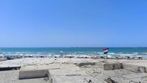 Una playa con una bandera, zona arenosa y cielo despejado.