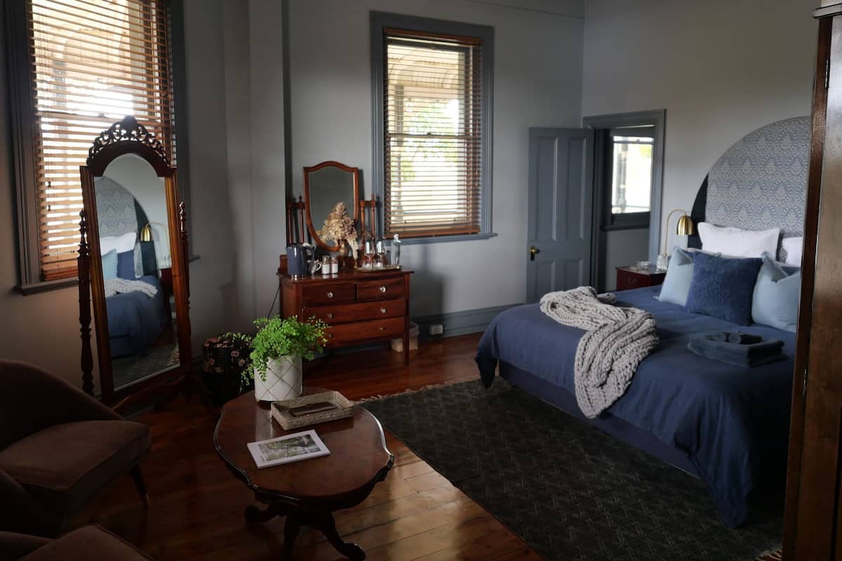 Quarto com cama, cômoda, espelho e janela com persianas.
