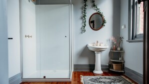 A bathroom with a glass shower door, a pedestal sink, and a mirror on the wall.