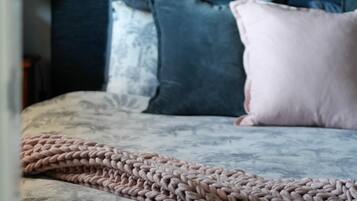 A bed with a patterned duvet cover, a knitted throw blanket, and multiple pillows in shades of blue and pink.