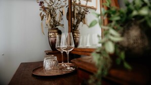 A wooden table with a tray holding wine glasses and small glass jars, with dried flowers in the background.