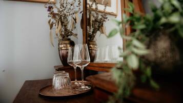 A wooden table with a tray holding wine glasses and small glass jars, with dried flowers in the background.