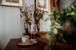 A wooden table with a tray holding wine glasses and small glass jars, with dried flowers in the background.