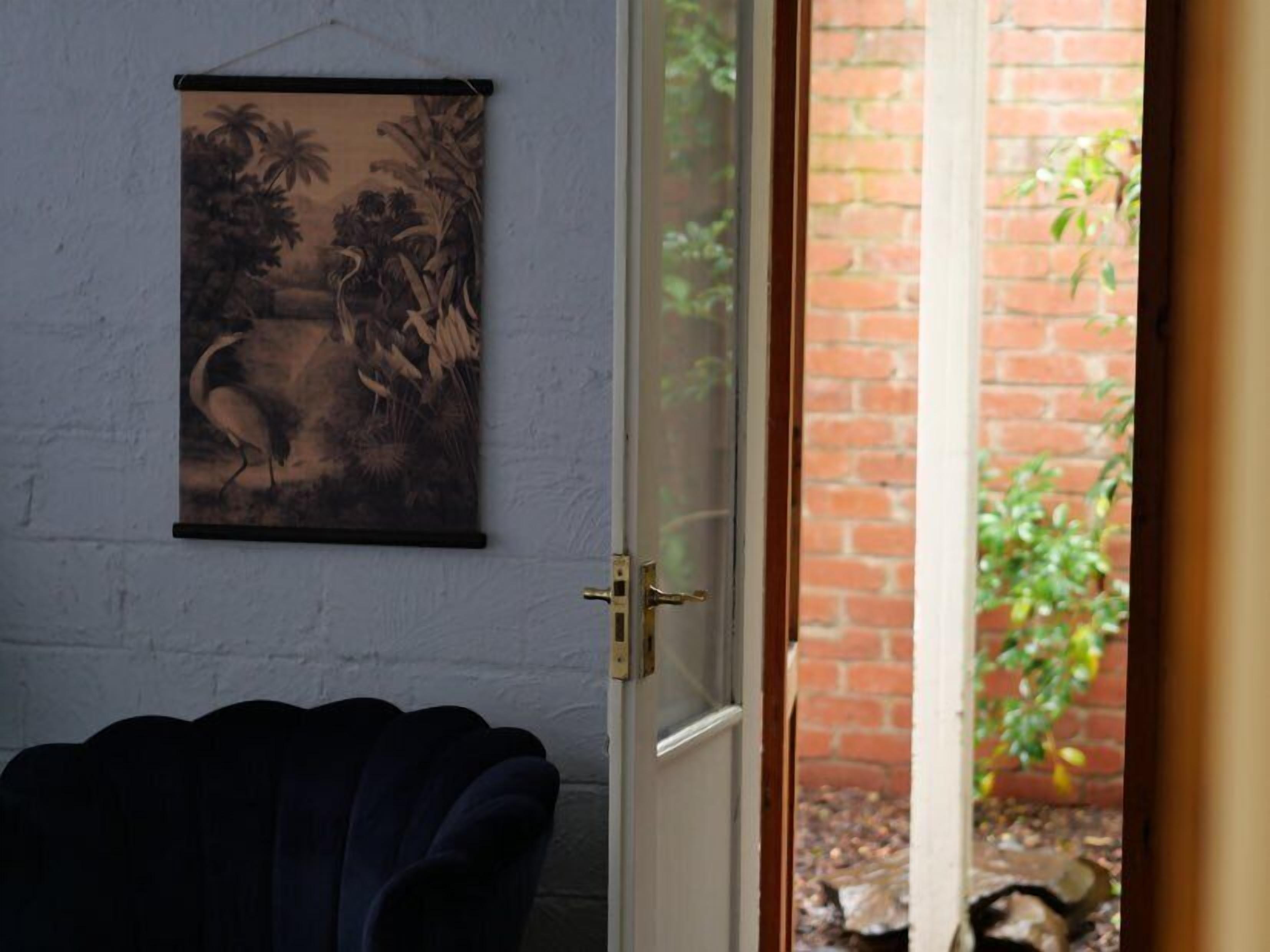 Una habitación con una silla azul oscuro, una puerta con picaporte de latón y un cuadro colgado en la pared de un paisaje.