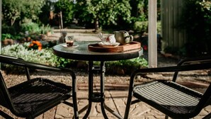 A round table with a pitcher, teacup, and saucer, and two wicker chairs in a garden setting. - The Rabbit Hole Inn at Harvest Home (Avenel)
