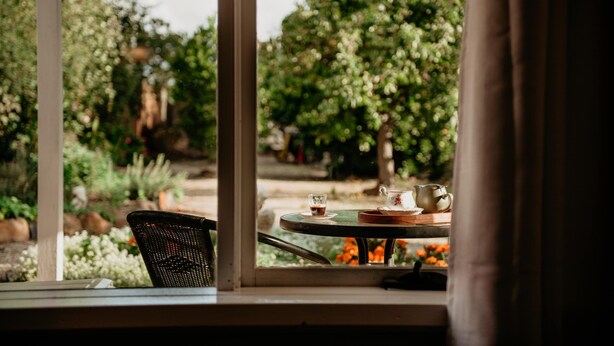 A view from a window with a table set for two, featuring a cup and saucer, a teapot, and a tray. - The Rabbit Hole Inn at Harvest Home (Avenel)