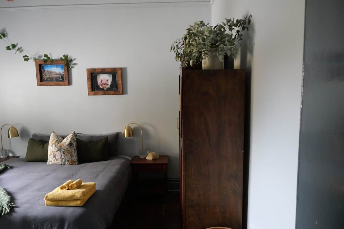 Quarto com cama, duas mesas de cabeceira, um criado-mudo, um guarda-roupa de madeira e duas quadros na parede.