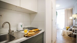 Una cocina moderna con un lavamanos de acero inoxidable, una tetera, una tabla de cortar con queso y pan, y una tableta en la encimera.