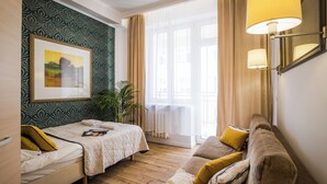 Habitación de hotel con cama, sofá, ventana con cortinas, una planta y un cuadro en la pared.