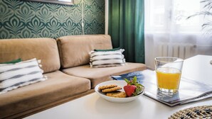 Una sala de estar con un sofá, un tazón de galletas y una fresa, y un vaso de jugo de naranja sobre una mesa.