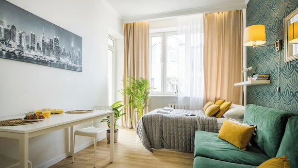 Una habitación de hotel moderna con una cama, un sofá verde, una mesa de comedor con sillas y un cuadro de paisaje urbano en la pared.