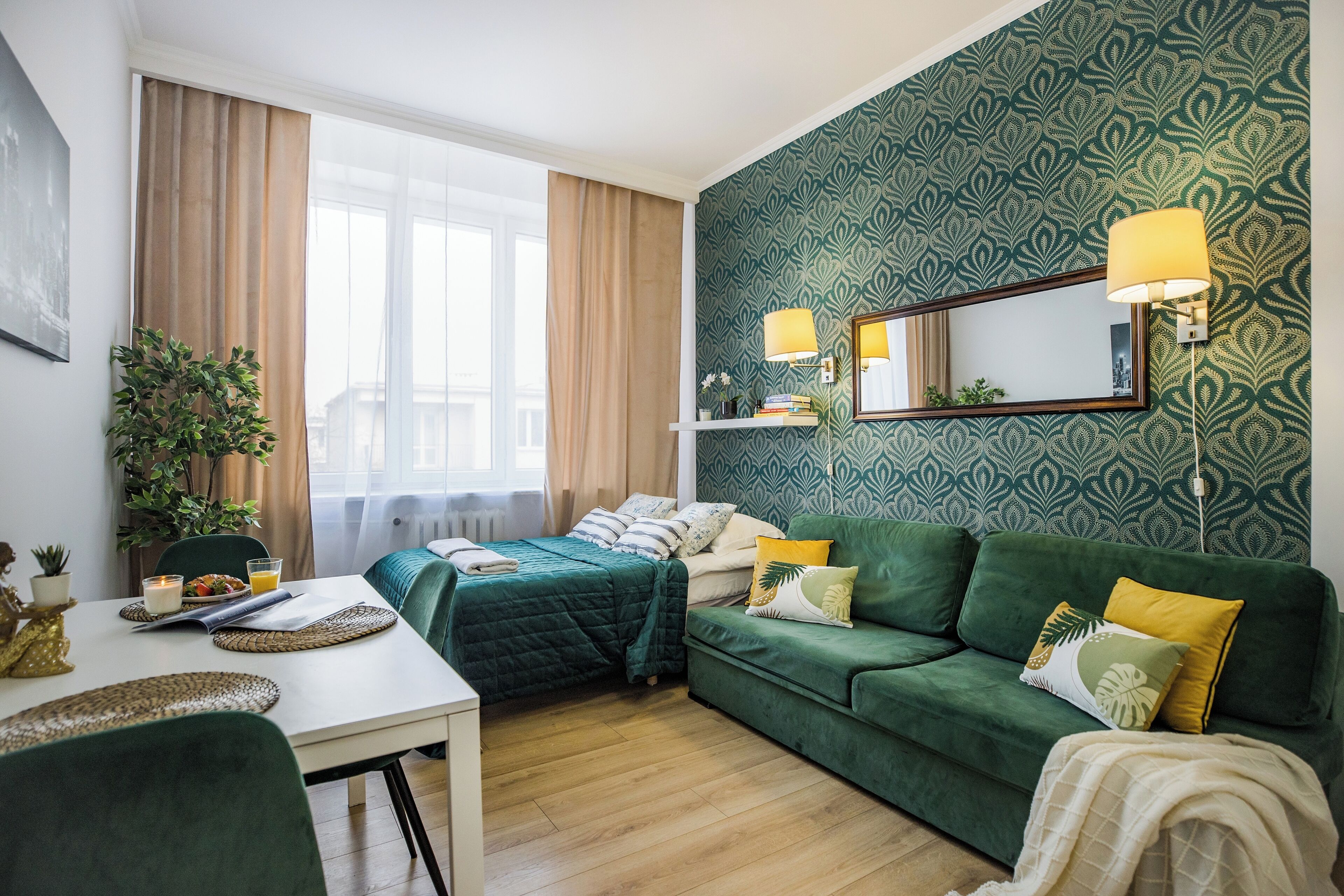 Una stanza con un letto, un divano verde, un tavolo da pranzo e un'ampia finestra con tende.