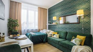 Una stanza con un letto, un divano verde, un tavolo da pranzo e un'ampia finestra con tende.