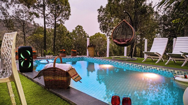 Una piscina con sillas de descanso y una hamaca, rodeada de árboles.