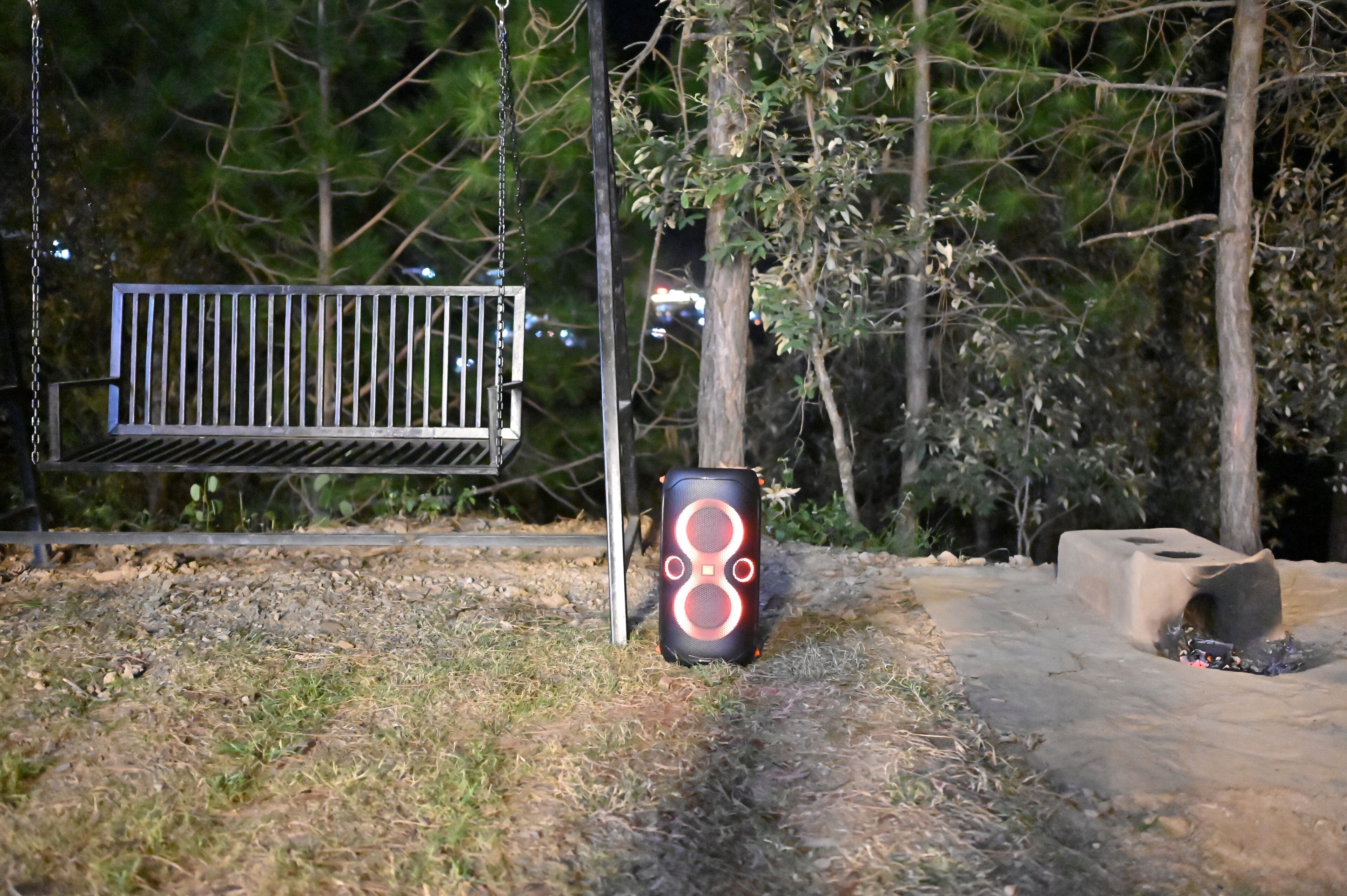 En bänk av metall och ett cylindriskt föremål med ett lysande mönster, placerade i ett skogsområde med en gångstig av betong.