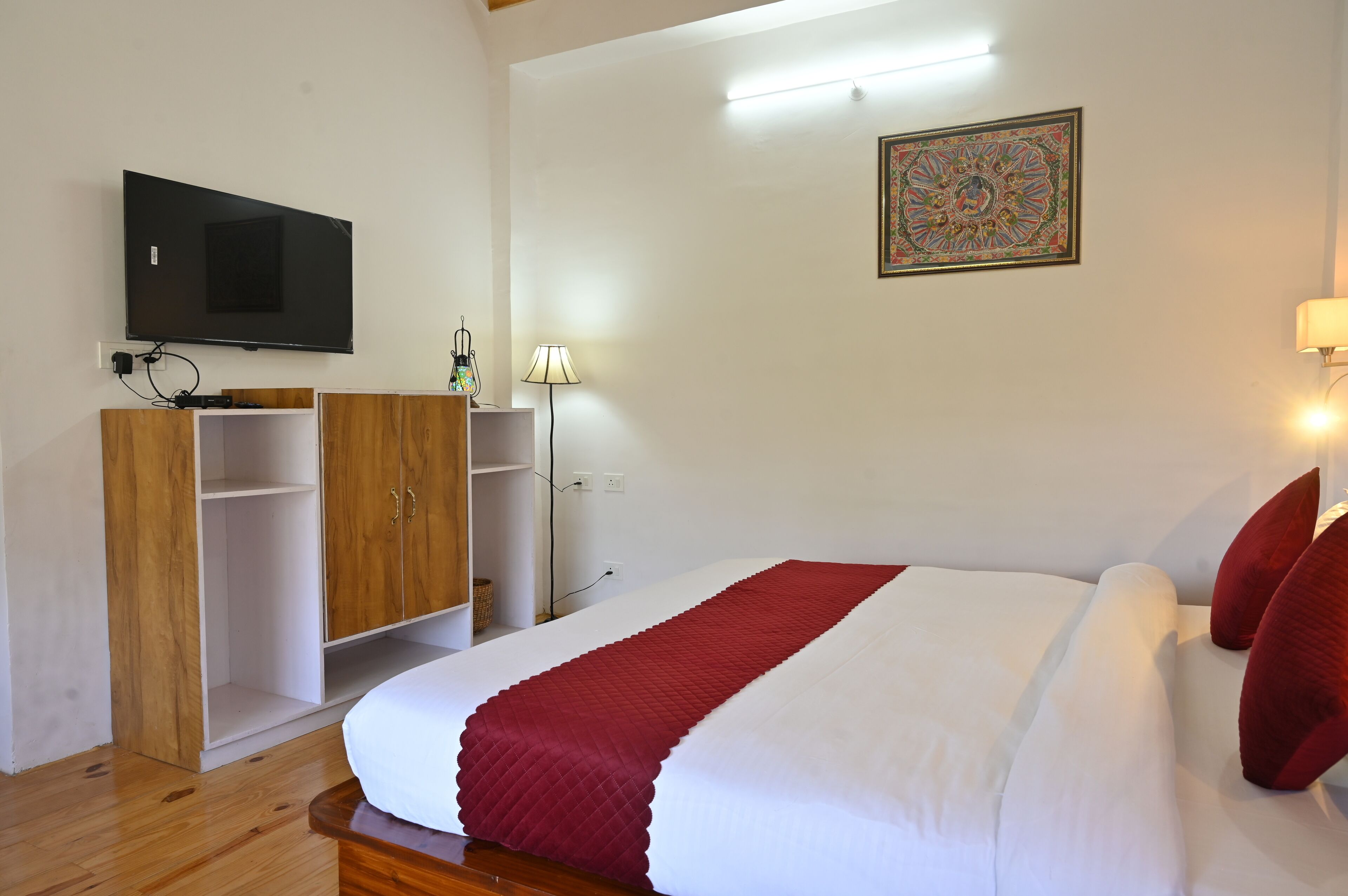 Un dormitorio con una cama, un televisor fijado a la pared, un armario y una lámpara.
