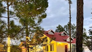 Una casa de dos pisos con techo rojo, rodeada de árboles y un patio cubierto de césped.