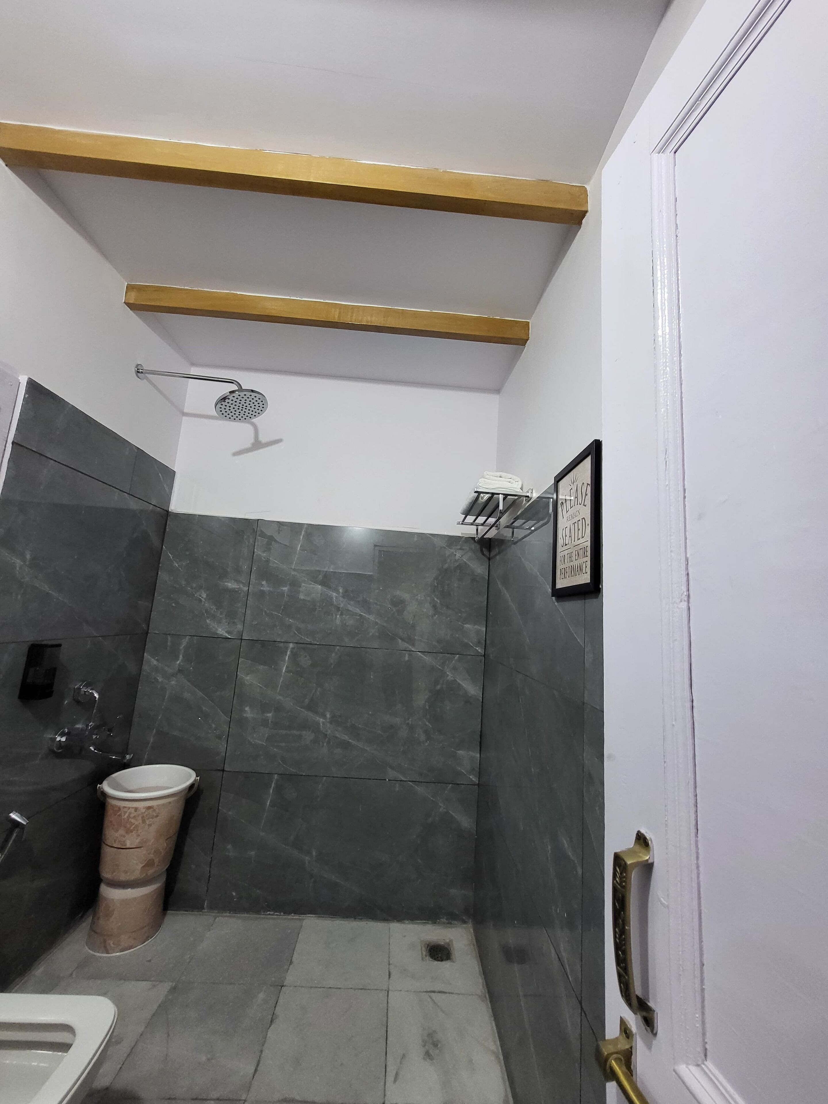 A compact bathroom with dark marble tiles, a shower with a handheld showerhead, a toilet, and a sink.