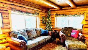 A cozy log cabin interior with a leather sofa, a patterned armchair, and a small wooden table. - Elk City Escape - Amazing Views, Elk, & Wildlife (Elk City)