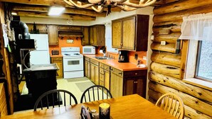 A rustic cabin interior with a wooden dining table, chairs, a kitchen with a stove, microwave, and cabinets. - Elk City Escape - Amazing Views, Elk, & Wildlife (Elk City)