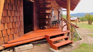A log cabin with a wooden porch, a bench, and a staircase leading to the entrance. - Elk City Escape - Amazing Views, Elk, & Wildlife (Elk City)